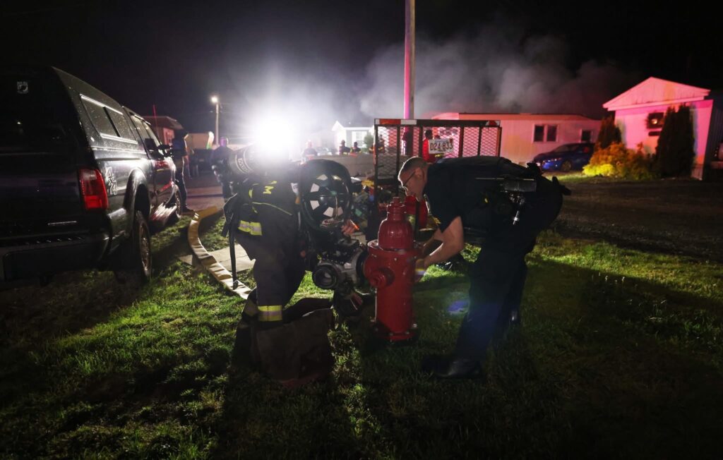 Raynham Fire and Raynham Police work together to open a fire hydrant at the scene of a mobile home fire on Broadway on Sunday night. 